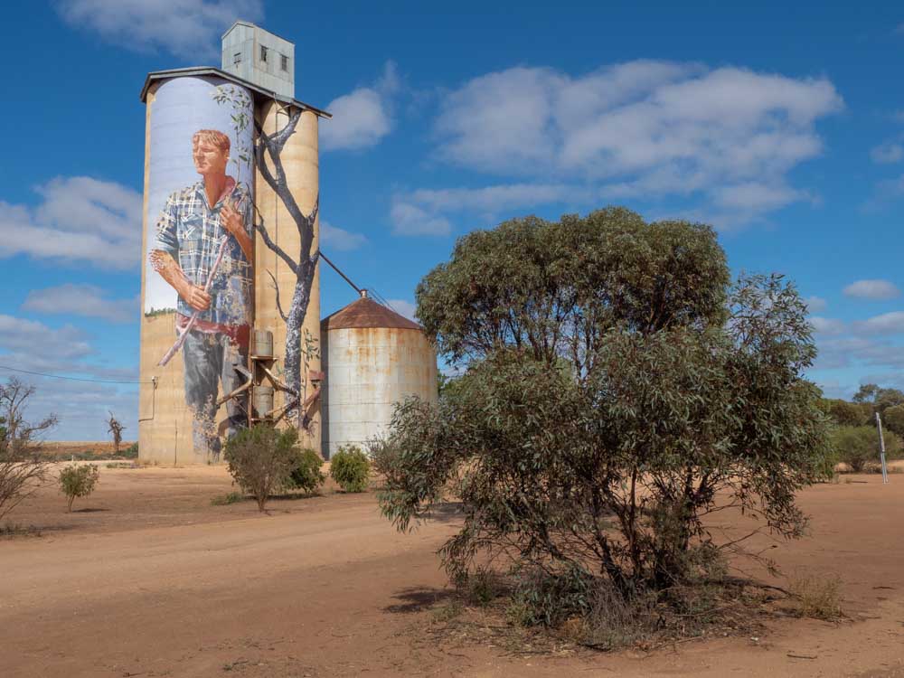 Painted silos of Victoria Australia, FIntan Magee mural of a farmer with a bush
