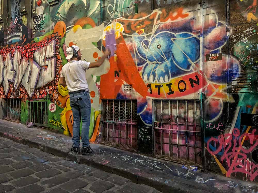 Graffiti Melbourne: Hosier Lane - man spray painting orange paint onto a wall