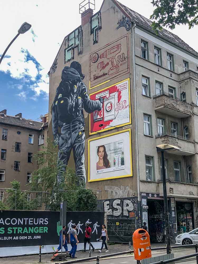 Berlin mural by MTO- Publicity. Man in hoodie and ads on a wall