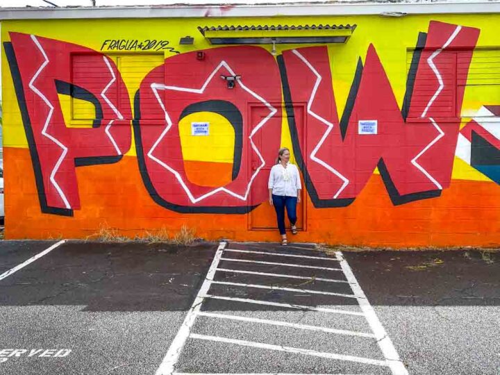 POW!WOW! Hawaii street art mural. Woman standing against a red and yellow mural