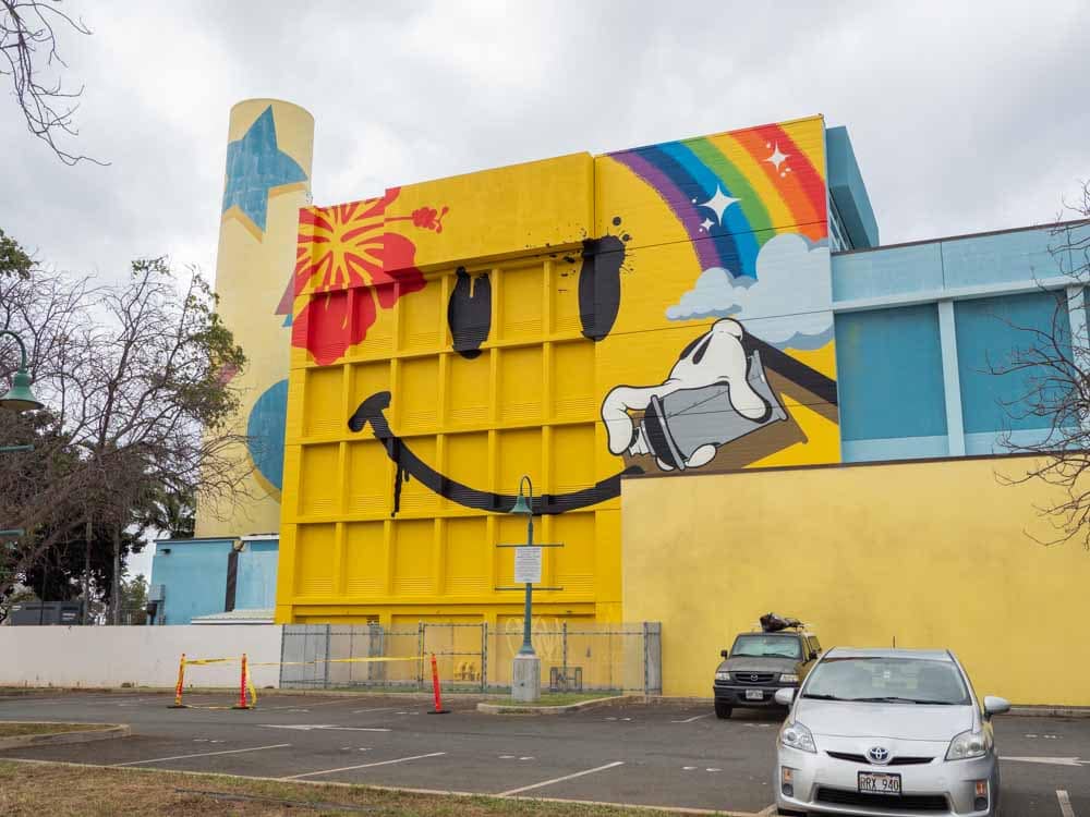 Kakaako street art mural by OG Slick- happy face. Yellow happy face and rainbow on a wall
